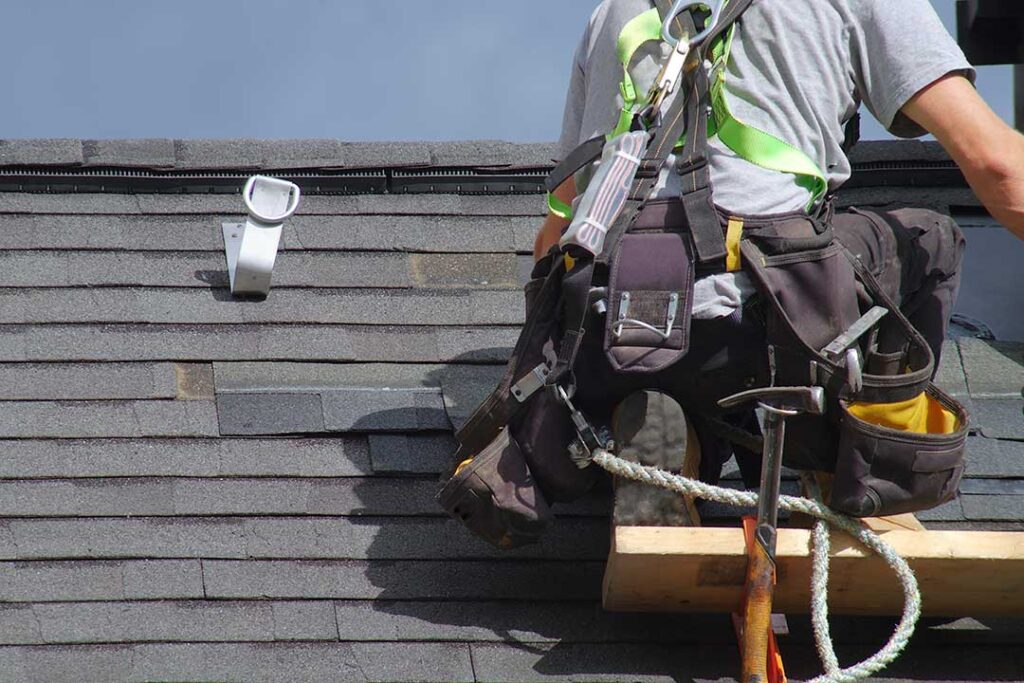 Homeowner reviews a roofing estimate with a contractor beside a house roof and inspection materials.